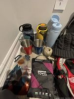 Photo of water bottles, stainless steel camping cups, quick-dry microfiber towel, knitted beanie, nylon cord, and North Face small backpack portion visible
