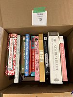 View of 11 cookbooks inside a cardboard box showing the spines with titles and authors visible
