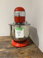 Close-up of the red stand mixer with stainless steel bowl on old wooden surface.