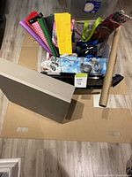 Top view of assorted gift-wrapping supplies arranged in a plastic bin including colorful bags, tissue papers, ribbons, box, bubble wrap, and wrapping paper roll.