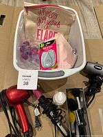 The lot of hair dryers, curling iron, makeup brushes, and cosmetic bags shown inside a plastic bin on cardboard.
