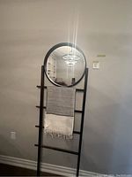 Full view of the round mirror hung on the decorative ladder with a striped cotton throw draped on ladder rung, showcasing mirror diameter and throw pattern.