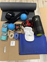 Overview view of all items on cardboard, showing yoga mats, Pilates balls, resistance bands, yoga straps, foam roller, heating pads, hand grips and white cap.