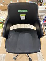 Top view of black upholstered office chair with walnut veneer on sides and back. Shows seat with small spot and backrest with wide curved design.
