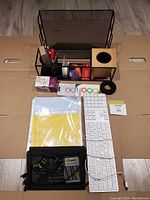 Top view of all items in the lot arranged on cardboard, showing keyboard, file tray, pen holder, tape roll, cable rings, and other supplies.