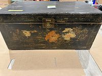 Front view of the black distressed vintage trunk showing floral designs and brass latch.