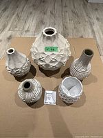 Front view of 5 West Elm textured vases on cardboard, showing scale and detail.