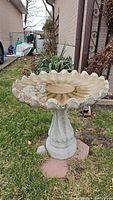 Front and angled view of concrete bird bath with scalloped edge basin placed outdoors on grass.