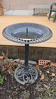 Front view of black metal bird bath showing ornate base and shallow bowl with twisted finial.