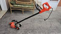 Full view of the Black & Decker Edge Hog landscape edger showing orange motor housing, black handle, and wheels.