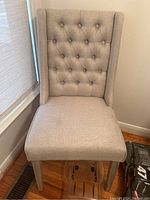 Front view of single beige button tufted side chair showing fabric upholstery, padded seat, and decorative backrest.