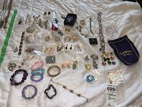 Overview of all jewellery items laid out on white cloth showing bracelets, rings, earrings, chain necklace, small pouch with earrings, and other accessories.