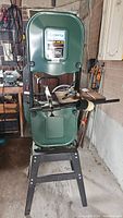 Front view of green Craftex band saw on black metal stand in garage