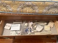 Drawer view showing assorted electrical accessories including timers, power bars, outlet extenders, and night lights scattered on drawer surface.