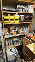 Overall view of 4 wooden shelves holding various hardware items in bins, boxes, and jars with a white dehumidifier on the floor in front.