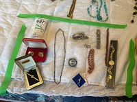 Full view of the assortment of men's costume jewellery items laid out on a cloth background including cuff links, bracelets, chains, and a Timex watch face.