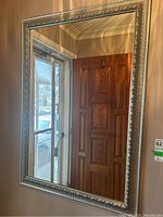 Frontal view of the large rectangular mirror hanging on a wall, showing the reflective surface capturing a wooden door and window in the background.