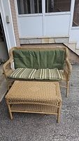 Wicker two-seater outdoor sofa with green and striped cushions shown from the front on a driveway.