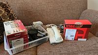 Overview of the lot showing a white GE corded phone, a basket with multiple cordless handsets, power cords, and a boxed VTech 2326 cordless phone system.