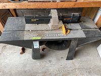 Front view of the Sears Craftsman Professional router table on angled legs with dust collection hose beneath and taped label.