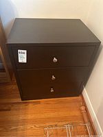 Front view of one dark wood side table showing three drawers with metal knob pulls and some chips to wood surface.