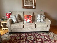 Front view of beige 3-seater sofa with cushions and 3 toss pillows, showing fabric texture and wood veneer base.