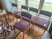 Six chairs arranged in two rows by window on hardwood floor with some contents placed on chairs and floor.