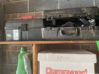 Closed black hard plastic and black plastic toolboxes on a wood shelf against a brick wall