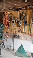 Wide view of pegboard wall in garage displaying various hanging tools including rakes, saws, handles, extension cords, and broom.