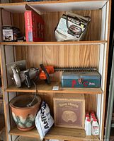 Overview of wooden shelves with tools including hedge trimmer, circular saw, battery charger box, metal toolbox, ceramic planter, bag of granular material, and bottles.