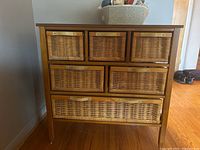Front view of wood veneer dresser with 6 wicker basket drawers showing their arrangement and brass-colored handles.