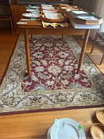 Wool area rug under a wooden table adorned with dishes and books, showing red floral center and beige border