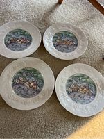 Four decorative plates with a picnic scene of cheeses and flowers in the center and embossed floral border showing details of design and condition.