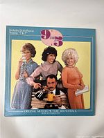 Front cover of the vinyl record for the '9 to 5' Original Motion Picture Soundtrack showing the main cast posing with props reflecting the 1970s office setting.