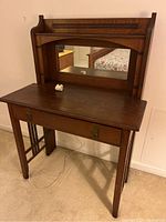 Front view showing the desk surface, drawer with metal handles, and mirror above.