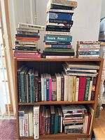Wooden bookshelf filled with multiple books from various genres on three shelves, showing general condition and arrangement.