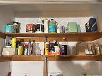 Wooden shelves holding assorted cleaning and household supplies including bottles, sprays, brushes, and boxes.