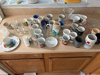 Overview of various cups, glasses, mugs, and dishes arranged on countertop.