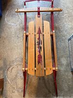 Top view of full sled showing wooden slats with arrow graphic and Flexible Flyer III branding on the crossbar, metal frame and runners, and attached yellow steering rope.
