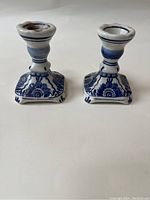 Front view of the two hand painted blue and white Delft ceramic candle holders showing floral motifs and square base.