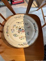 Close-up photo of one of the dinner plates showing cream color stoneware with floral and house pattern design.