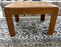 Front view of the square wooden coffee table showing rounded legs and wood grain finish on a patterned rug.