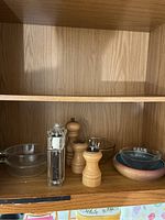 Wide photo showing shelf with Pyrex bowls, ceramic bowl, and variety of salt and pepper grinders and shakers