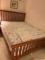 Photo showing wooden slatted queen bed frame with floral mattress and patchwork quilt folded on top.