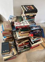 Photo showing multiple stacks of books with varied titles and the boxed Mind Trap puzzle game on top of one stack.