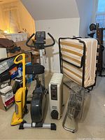 Wide view showing vacuum, exercise bike, heater, fan, folding bed frame and stacked shoe boxes