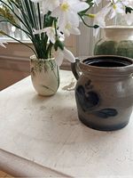 Photo of three items: Rowe Pottery crock, Kutani bamboo vase with flowers, and green glazed vase on a white table.