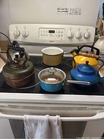 Full view of the 4 tea kettles and 2 small pots displayed on stovetop, showing color, shape, and condition for inventory.