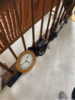 Clock leaning against stair rail showing the wooden frame and clock face with day display.