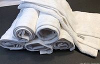 Six rolled white towels stacked with one towel unrolled showing texture and edges.